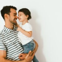 Funny happy dad and daughter play and cuddle together against white background. Good relationship of parent and child. Happy family moments of father and toddler girl. Childhood and parenthood care.
