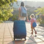 Young mother with daughter arriving at hotel, checking in, carrying luggage.