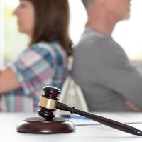 Divorce concept with judge gavel and couple sitting back to back in background, focus on foreground Divorce concept with judge gavel and couple sitting back to back in background, focus on foreground