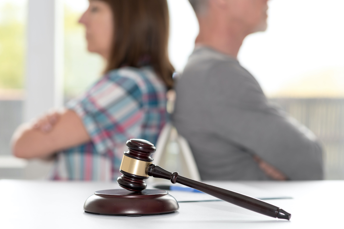 Divorce concept with judge gavel and couple sitting back to back in background, focus on foreground