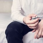 Concept of divorce and family disintegration. Man with wedding ring sitting in a marital bedroom, close up, cropped image, toned