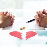 Couple's Hand On Divorce Paper With Wedding Rings And Broken Heart