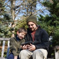 Young man and young boy sharing electronic device outdoors