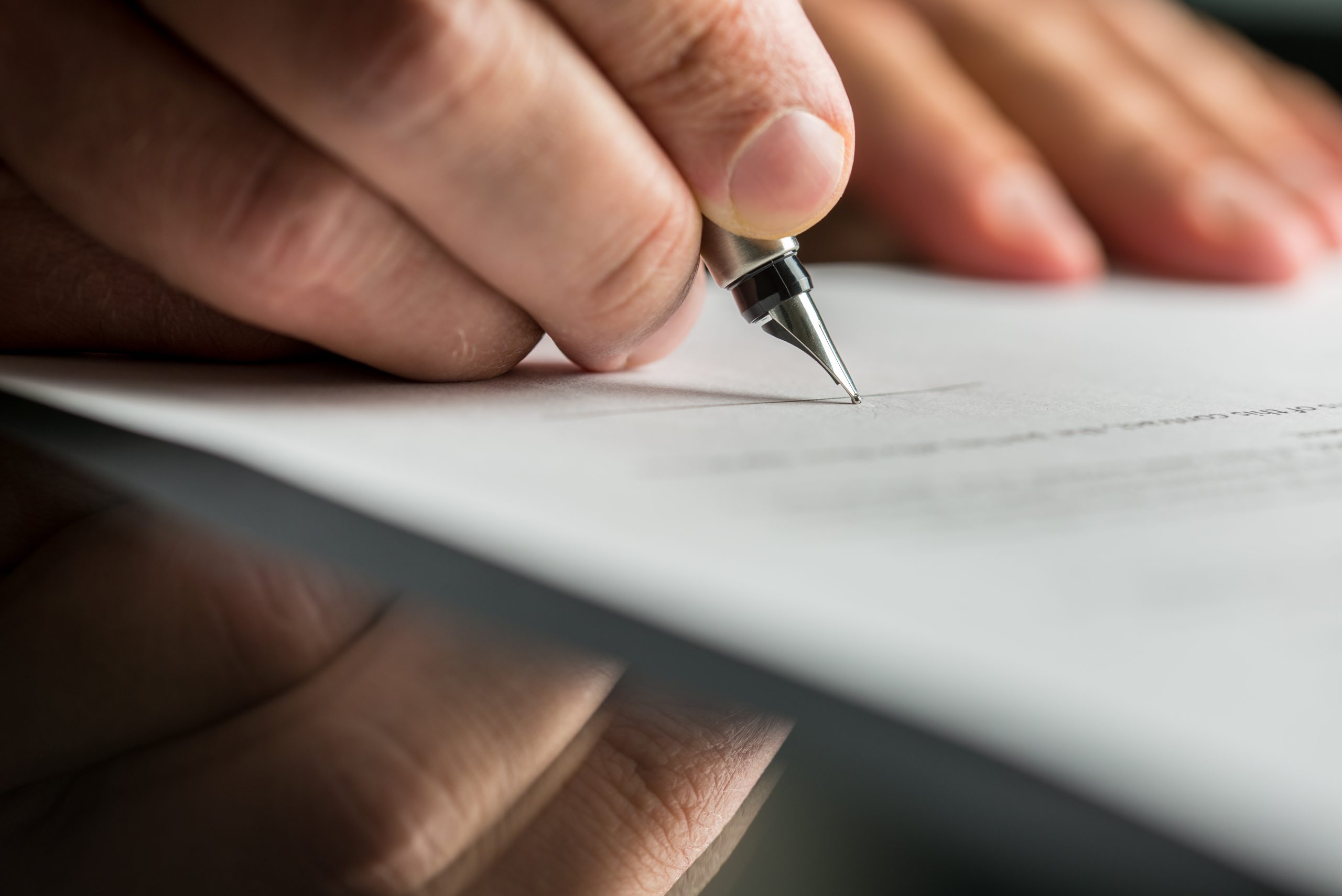 Closeup of male hand about to sign a will or a trust.