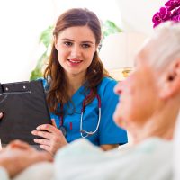 Kind nurse with clipboard in her hands registering senior woman's healthcare stats.