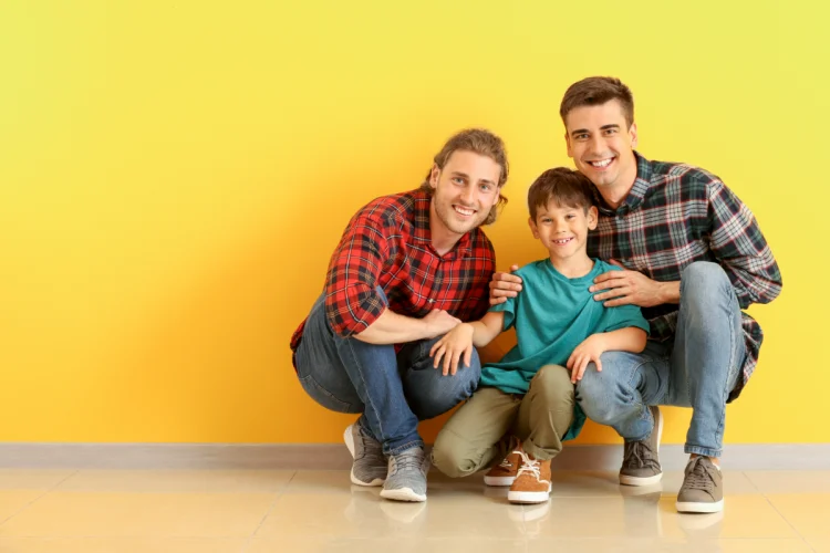 happy-gay-couple-with-adopted-child-near-color-wall